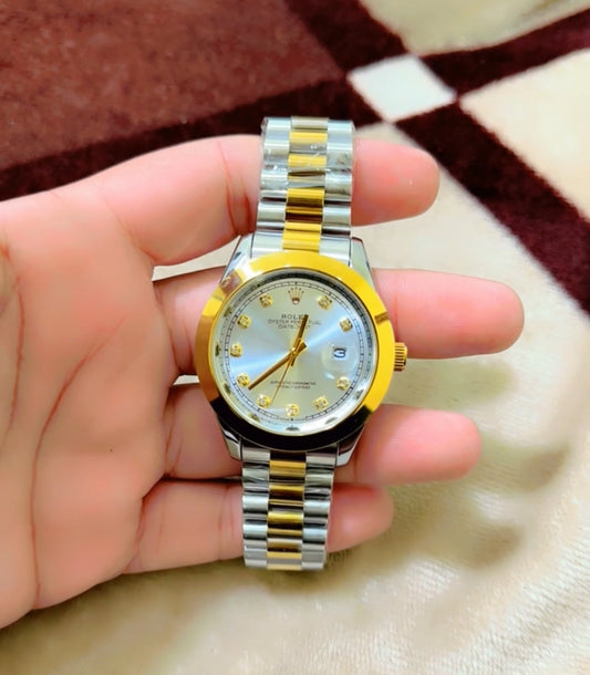 Two-tone watch with gold and silver straps held in a hand on a patterned fabric background